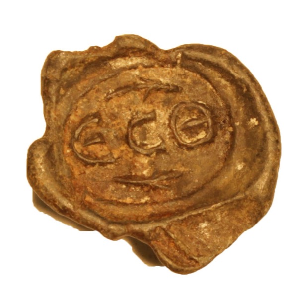 A Roman lead sealing — round lead disc stamped with Greek letters in a recessed cartouche, cord-lugs at the edge